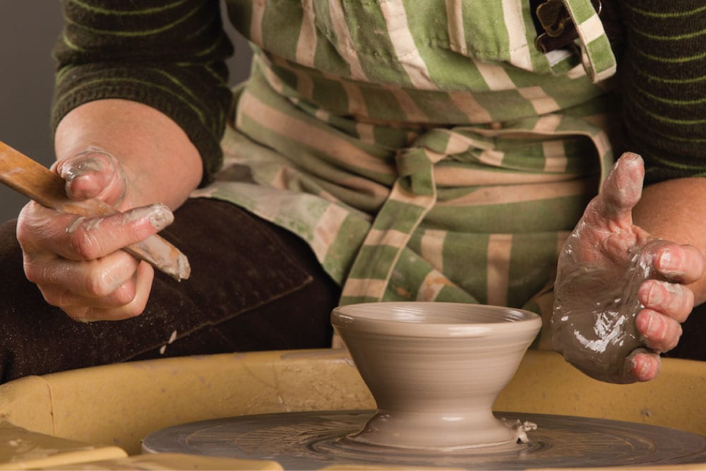 hands working on a clay pot on a pottery wheel
